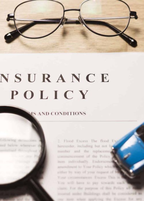 Insurance policy documents with eyeglasses, magnifying glass, paper clips, and a toy car on a desk.